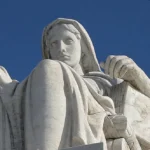 Escultura de una mujer sentada que sostiene un libro y una pequeña figura de la Justicia, representando la interpretación reflexiva del Derecho frente a la Corte Suprema de los Estados Unidos.