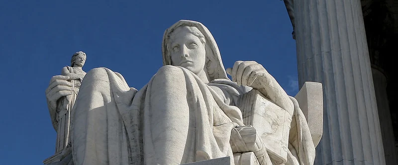 Sculpture of a seated woman holding a book and a small figure of Justice, representing thoughtful interpretation of law outside the U.S. Supreme Court.