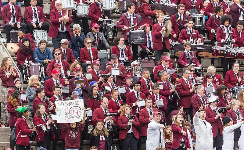 Des membres de la fanfare de l’université Harvard et d’anciens élèves se produisent lors d’un événement dynamique les jours de match, vêtus de leurs emblazers cramoisis emblématiques. Une démonstration vibrante de fierté universitaire et de tradition musicale. Crédit photo : Kenneth C. Zirkel (CC BY).