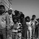 Niños esperando tras alambres de púas: una imagen de vulnerabilidad moldeada por condiciones sociales y políticas más amplias (CC0).