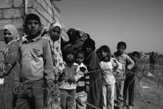 Des enfants attendant derrière des barbelés — une image de vulnérabilité façonnée par des conditions sociales et politiques plus larges (CC0).