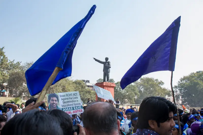 Des étudiants et militants dalits se rassemblent sous la statue de B. R. Ambedkar lors d’une manifestation réclamant justice pour Rohith Vemula et les victimes de la violence fondée sur les castes. Leurs banderoles demandent l’adoption d’une « Loi Rohith » pour lutter contre la discrimination systémique.  Photo de Joe Athialy (CC BY-NC-SA).