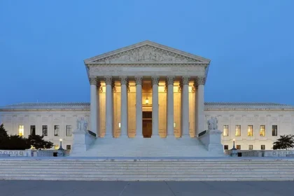 Supreme Court of the United States building at dusk in Washington, D.C., illuminated against a clear evening sky. Photo by Joe Ravi, CC BY-SA.
