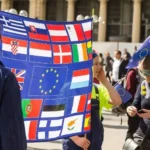 Protesters display a banner of national flags surrounding the European Union emblem during a pro-EU demonstration, reflecting the tension between national sovereignty and supranational integration that shapes debates over migration policy in Europe.