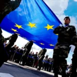 Soldiers carry the European flag during a military ceremony, a fitting image for a continent debating how far its war economy should reshape the symbols and structures of integration. Photo by European Parliament (CC BY-NC-ND)